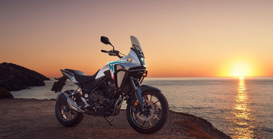 Honda NX500 blanche garée sur un chemin de terre au bord de la mer, au coucher du soleil.
